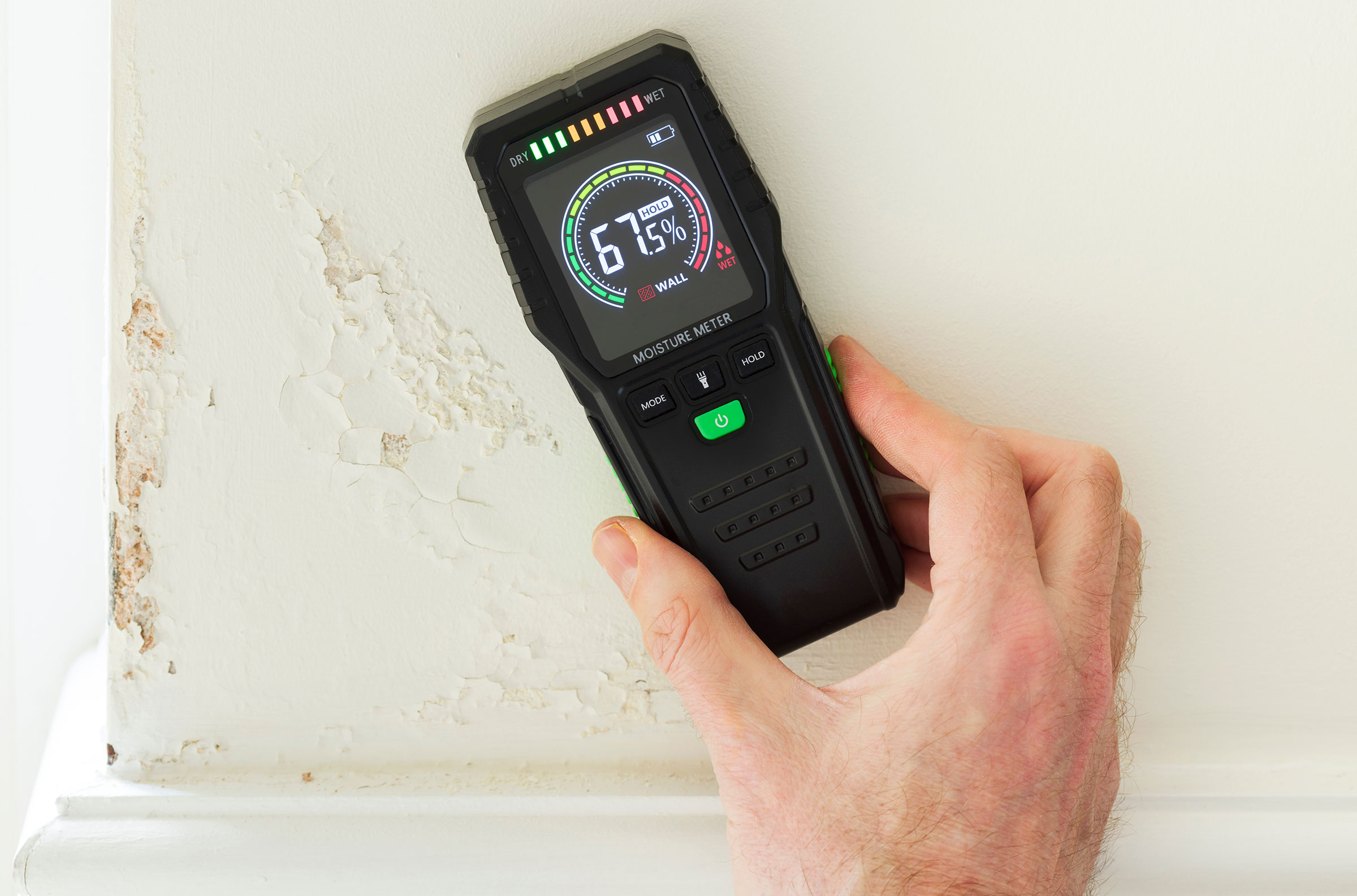 Moisture Meter being held up against a damp-damaged wall.